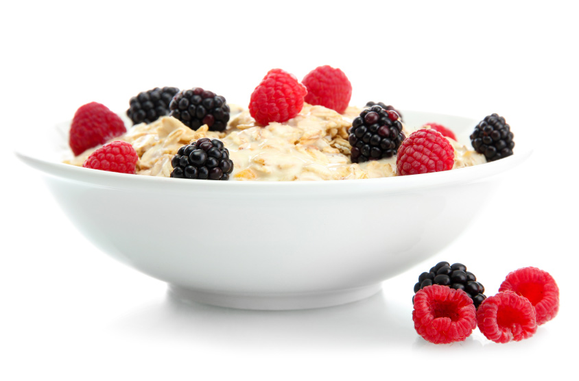 Porridge mit Beeren garniert in einer wei&szlig;en Sch&uuml;ssel vor wei&szlig;em Grund.