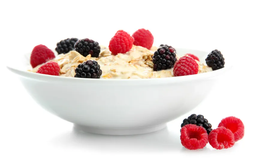 Porridge mit Beeren garniert in einer wei&szlig;en Sch&uuml;ssel vor wei&szlig;em Grund.