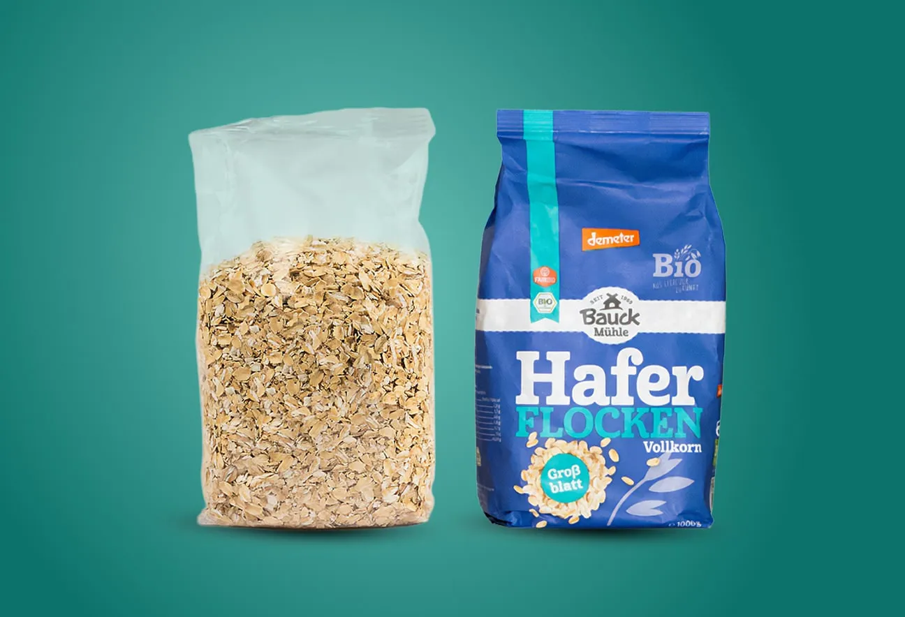 Transparenter Haferflockenbeutel und blaues Vollkorn-Haferflockenpaket nebeneinander vor gr&uuml;nem Hintergrund angeordnet