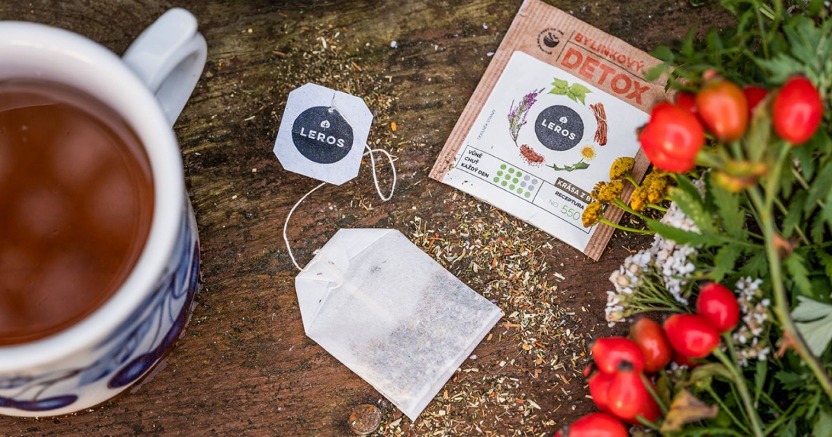 Tasse Kr&auml;utertee mit LEROS-Teebeutel, Detox-Packung und frischen roten Beeren sowie Kr&auml;utern auf rustikalem Holztisch