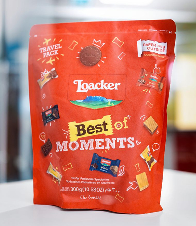 Rote Loacker-T&uuml;te Best of Moments steht auf wei&szlig;er Fl&auml;che, zeigt verschiedene Waffelriegel und Snacks im Reiseformat