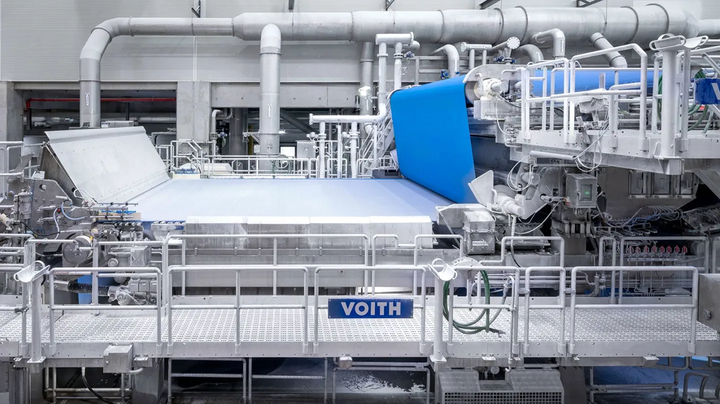 Moderne Papiermaschinenanlage mit breiter Produktionsbahn und markanter blauer Bahnf&uuml;hrung in heller Industrieumgebung
