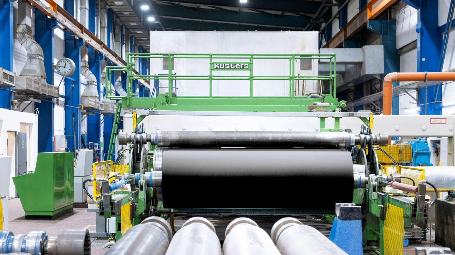 Industrielle Papiermaschinenanlage mit gro&szlig;en Walzen in weitl&auml;ufiger Produktionshalle