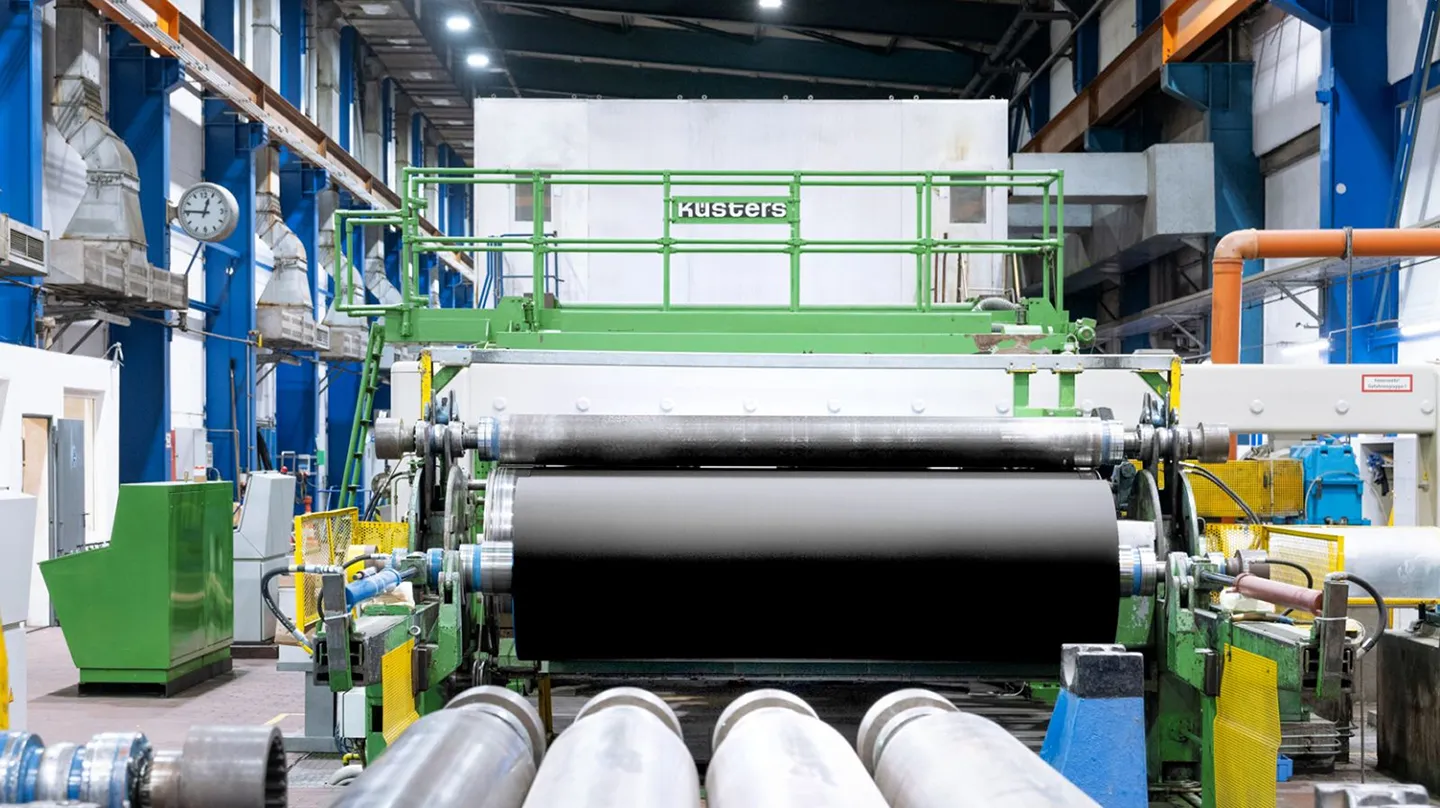 Industrielle Papiermaschinenanlage mit gro&szlig;en Walzen in weitl&auml;ufiger Produktionshalle