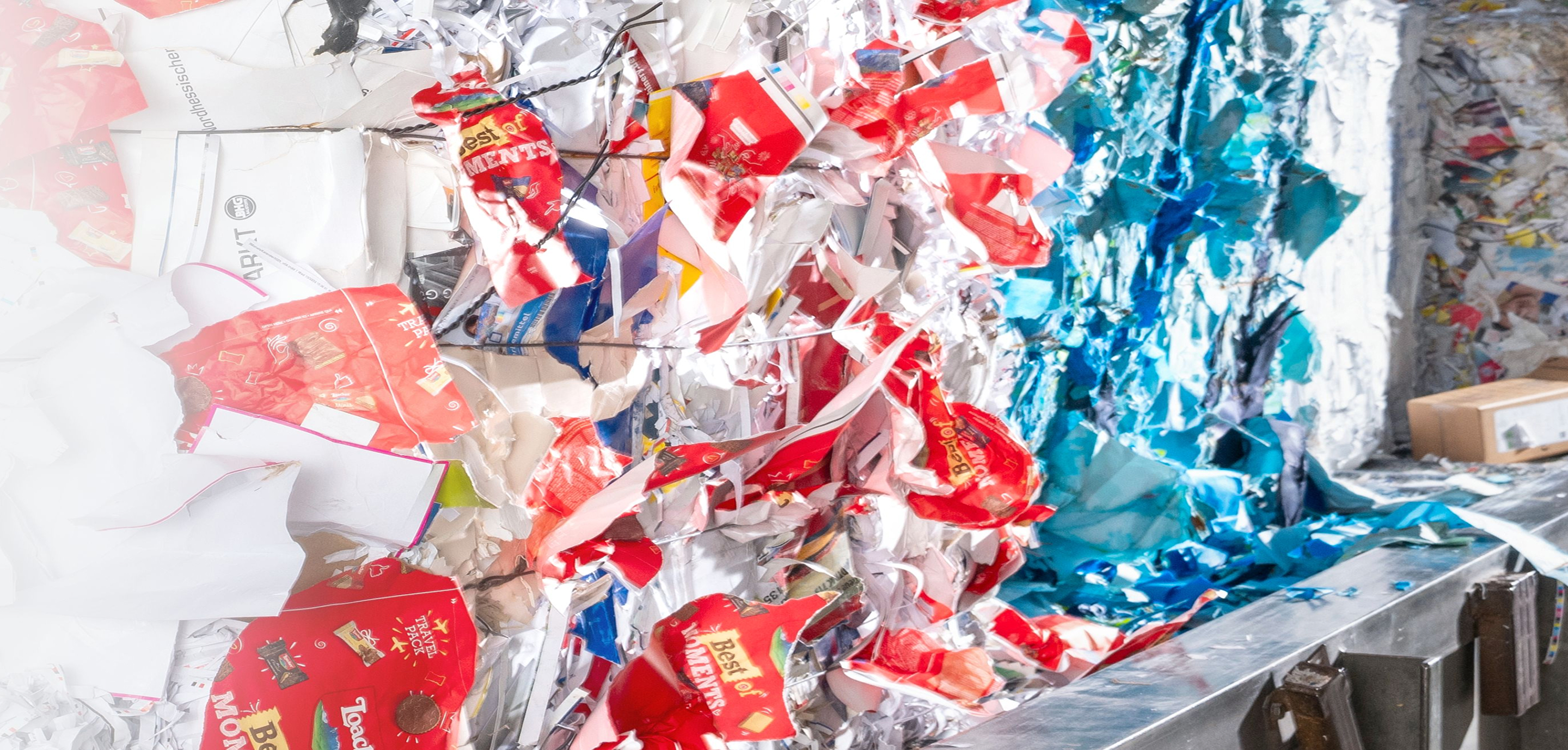 Verdichtete Ballen aus bunten recycelten Verpackungsresten in Rot‑, Blau‑ und Wei&szlig;t&ouml;nen in einer Sortieranlage