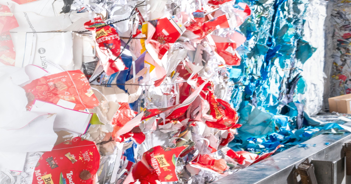 Verdichtete Ballen aus bunten recycelten Verpackungsresten in Rot‑, Blau‑ und Wei&szlig;t&ouml;nen in einer Sortieranlage