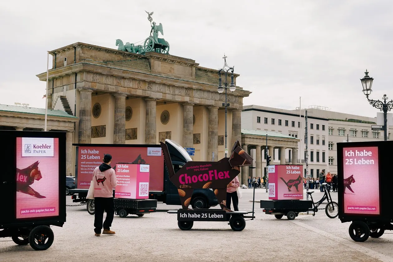 Vor dem Brandenburger Tor stehen pinke Werbefahrzeuge von Koehler Paper zur Kampagne "Pack's mit Papier" mit Slogan "Ich habe 25 Leben"