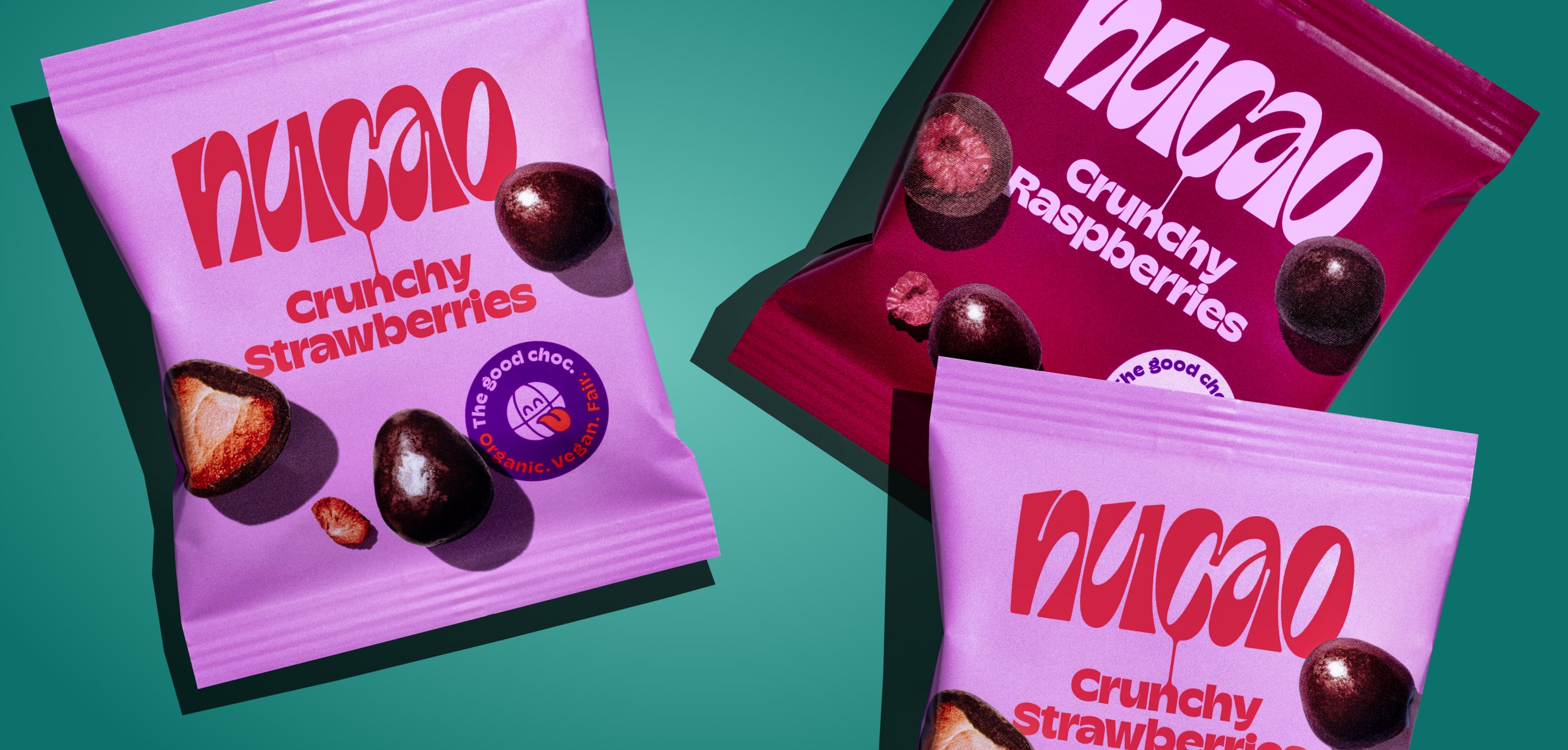 Bunte nucao-Snackbeutel f&uuml;r Mandeln, Erdbeeren und andere Sorten liegen verstreut auf t&uuml;rkisem Hintergrund mit N&uuml;ssen.